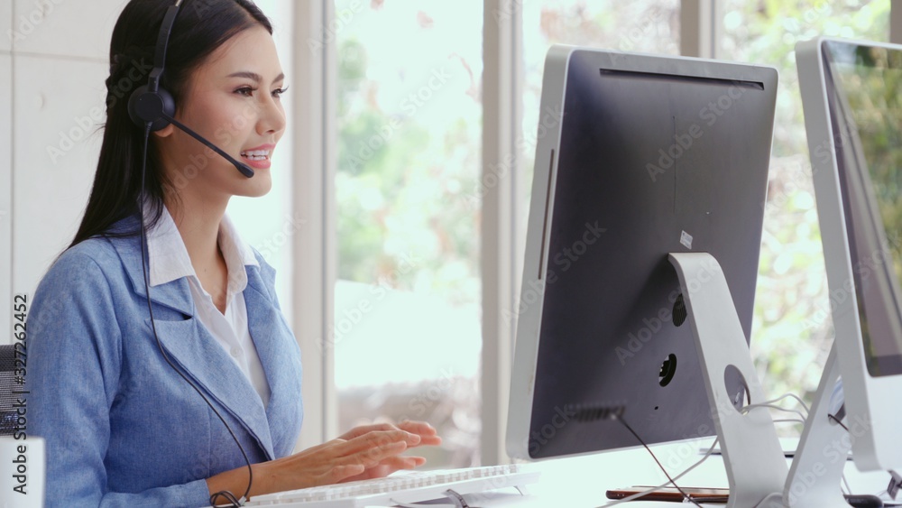 Customer support agent or call center with headset works on desktop computer while supporting the cu