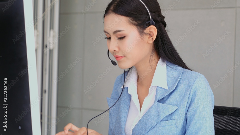 Customer support agent or call center with headset works on desktop computer while supporting the cu