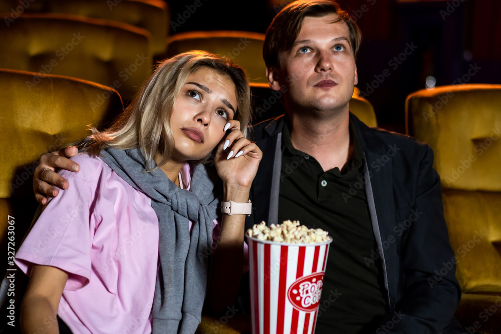 Caucasian man and woman watching a sad movie and his girlfriend crying