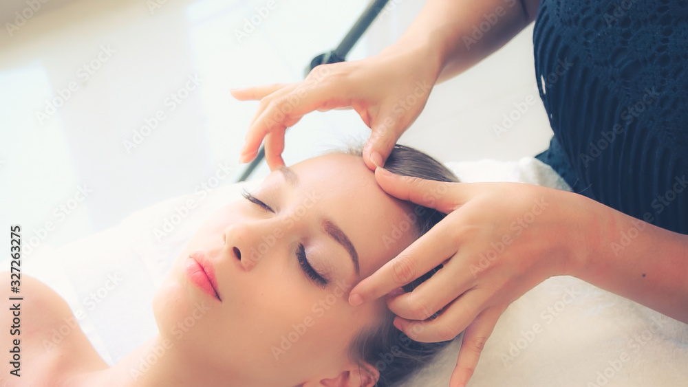 Relaxed woman lying on spa bed for facial and head massage spa treatment by massage therapist in a l