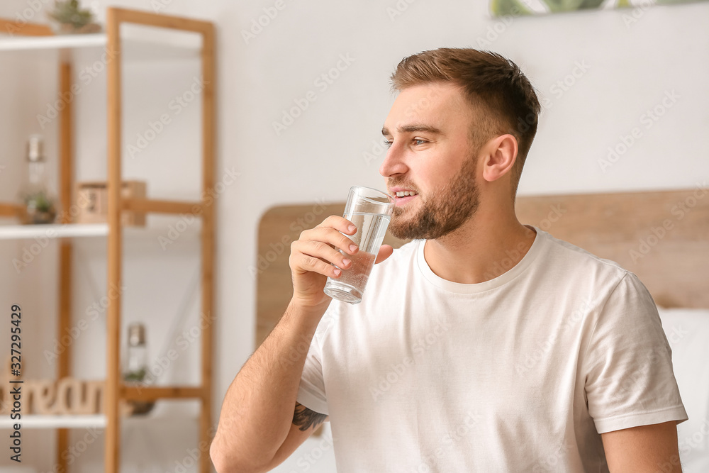 Morning of young man drinking water in bedroom