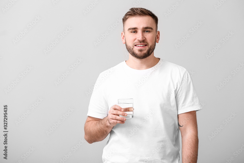 Young man with glass of water on light background