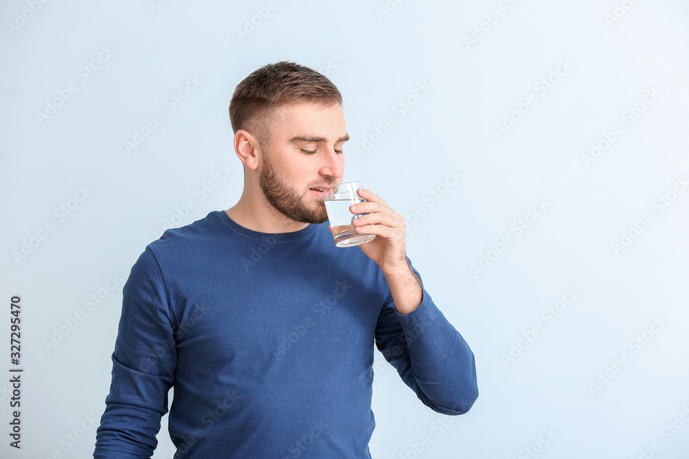 Young man with glass of water on light background