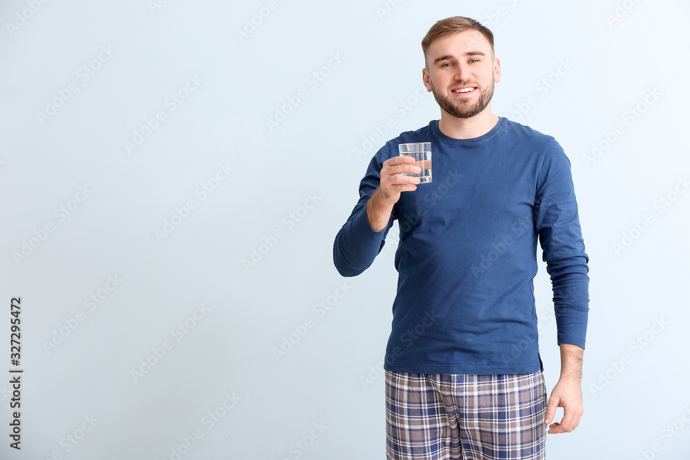 Young man with glass of water on light background