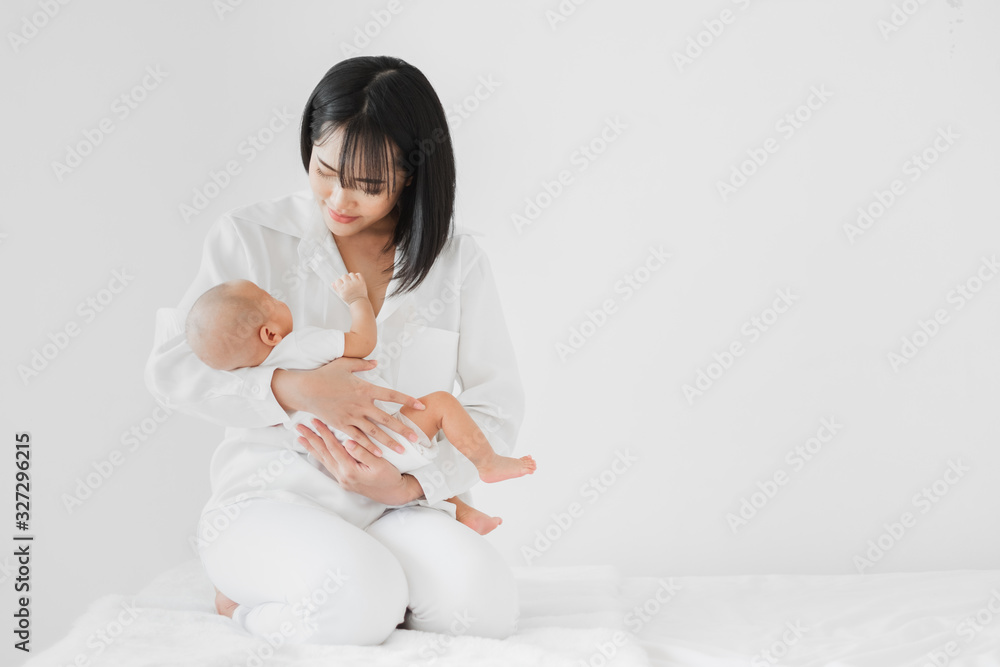 Young Asian mother holding her newborn baby with love on white bed, mothers day concept