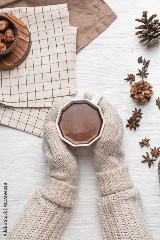 Female hands with cup of hot chocolate on white wooden background