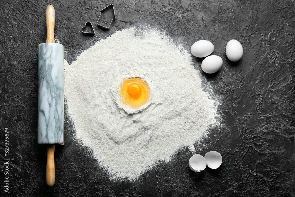 Ingredients for preparing cookies and rolling pin on dark background