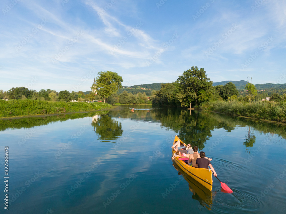 AERIAL: Flying behind tourists canoeing along calm river running past a church