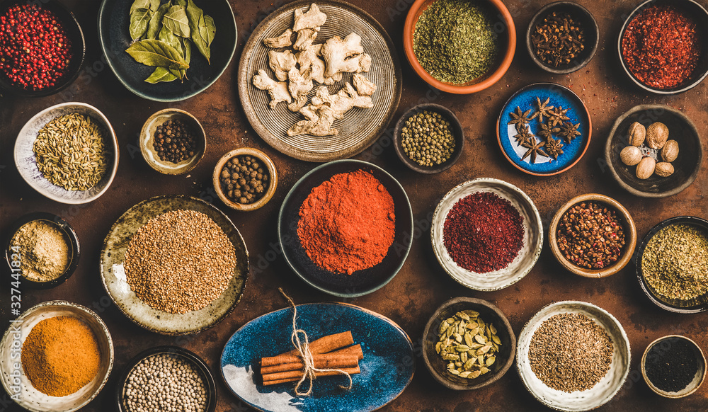 Flat-lay of spices in bowls and plates over rusty background, top view. Black pepper, allspice, clov