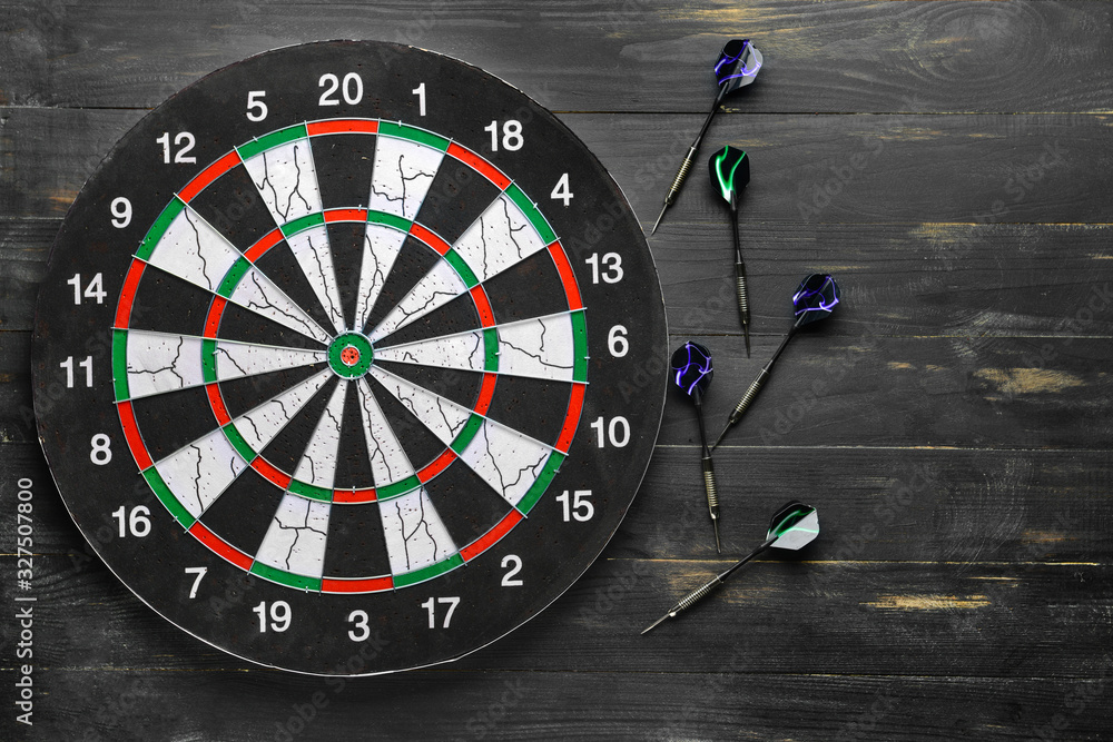 Dartboard with darts on dark wooden background