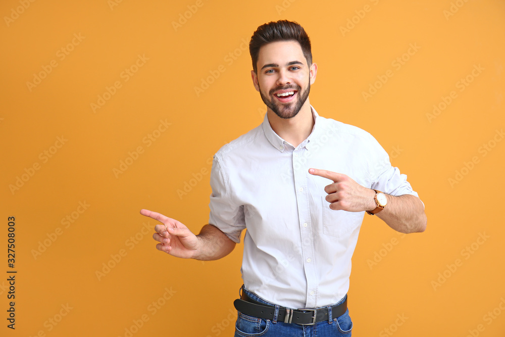 Handsome young man pointing at something on color background