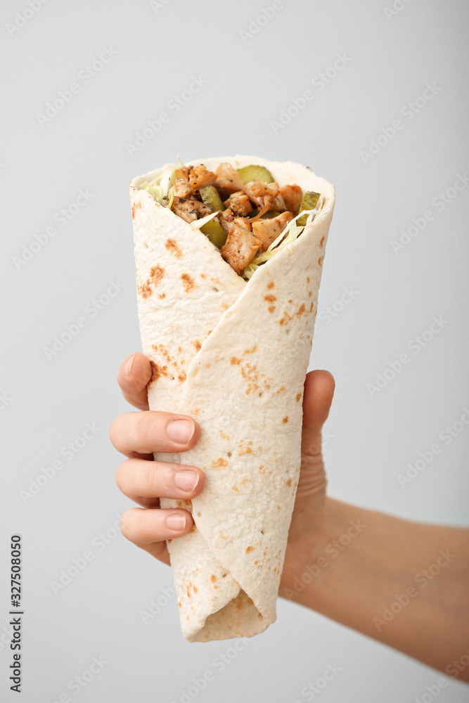 Female hand with tasty doner kebab on light background