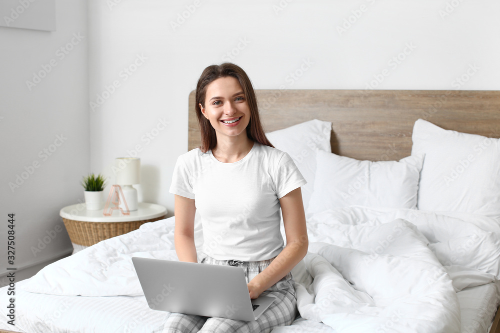 Morning of beautiful young woman with laptop in bedroom