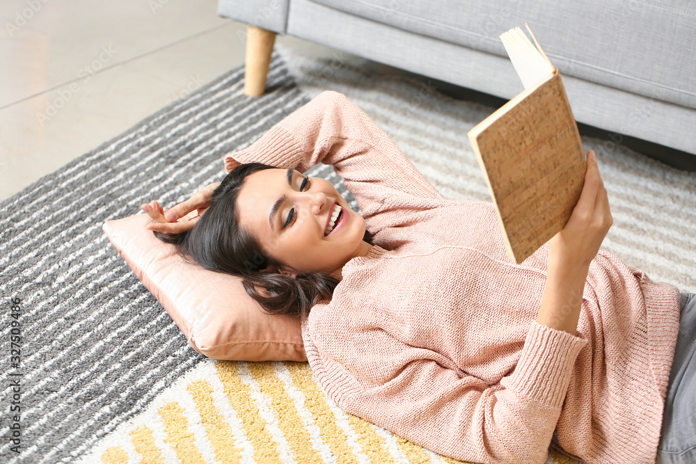 Beautiful young woman in warm sweater reading book at home