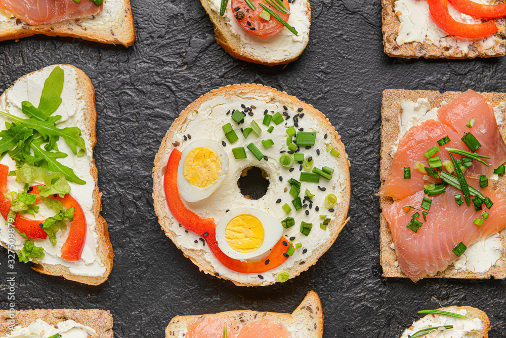 Different sandwiches with tasty cream cheese on dark background