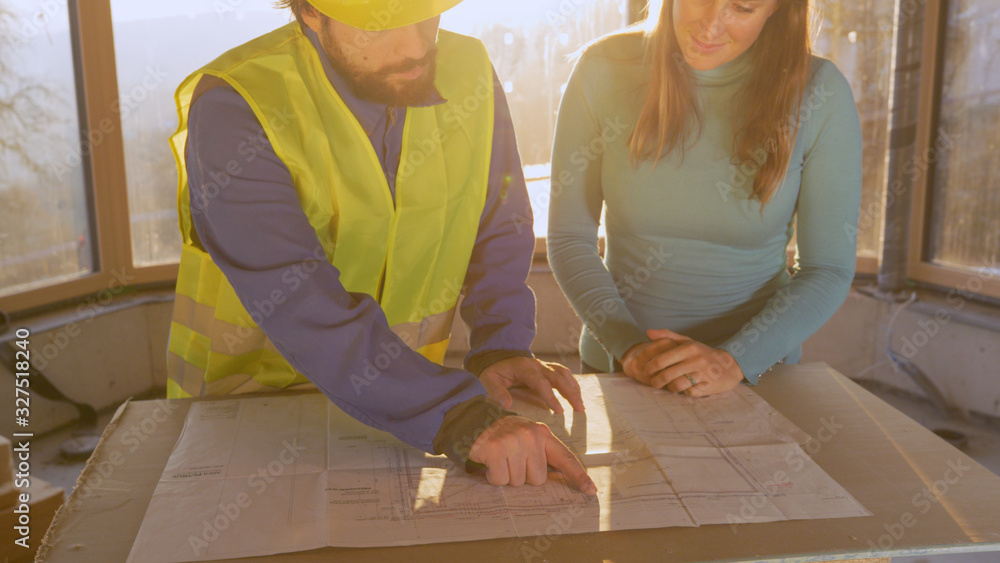 CLOSE UP: Woman listens to architect explaining the floor plans at sunrise.