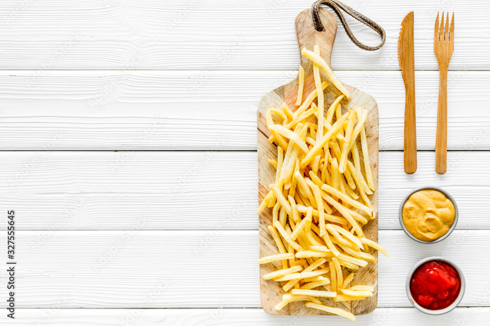 Fast food restaurant concept. French fries on cutting board near sauces on white wooden table top-do