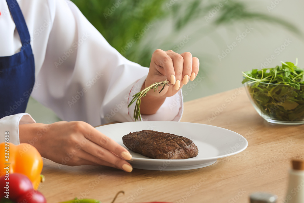 Female chef adding herbs to tasty meat in kitchen, closeup