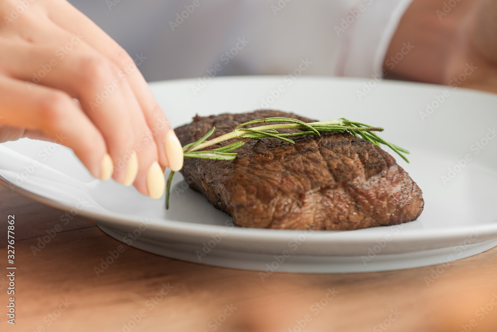 Female chef adding herbs to tasty meat in kitchen, closeup