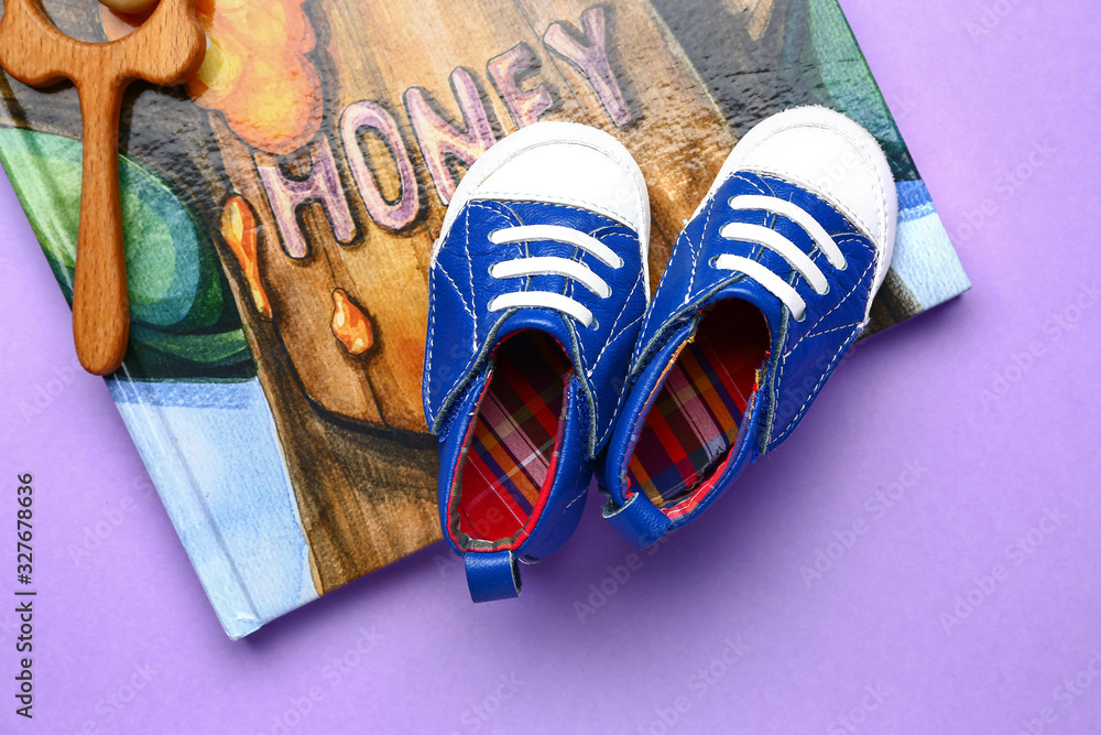 Baby booties with toy and book on color background