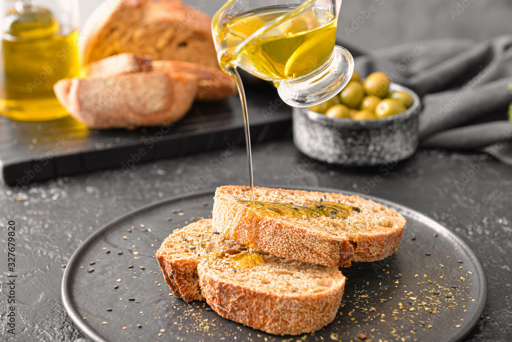 Pouring of tasty olive oil from gravy boat on fresh bread