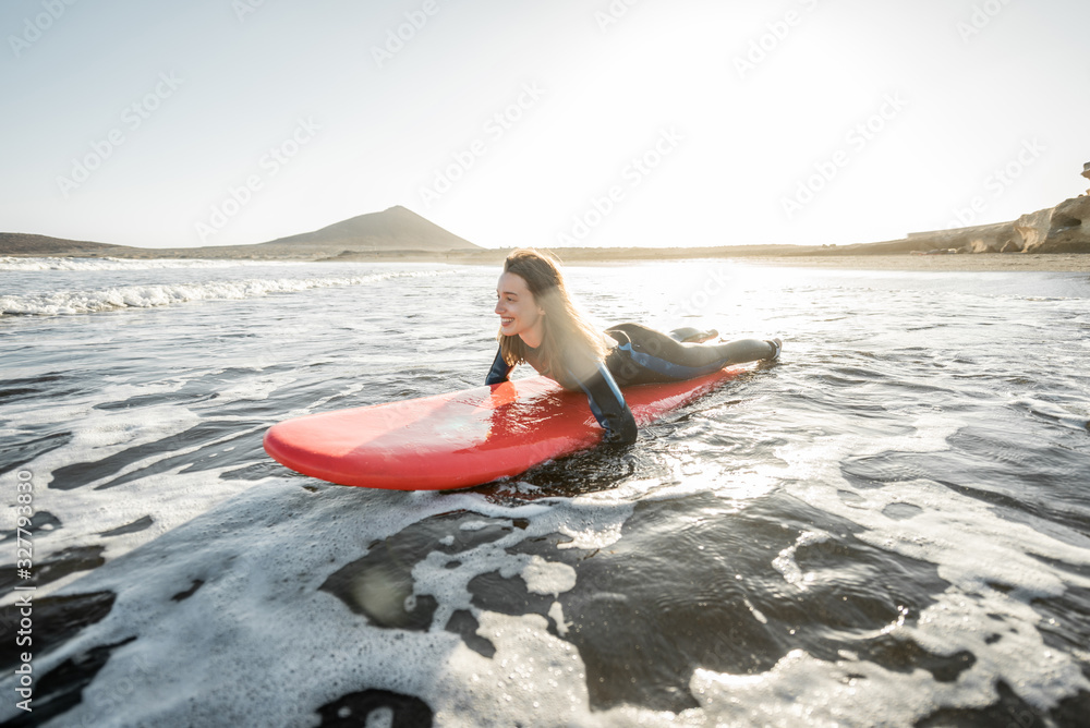 Young woman in wetsuit catching water flow on the surfboard, surfing on the wavy ocean during a suns