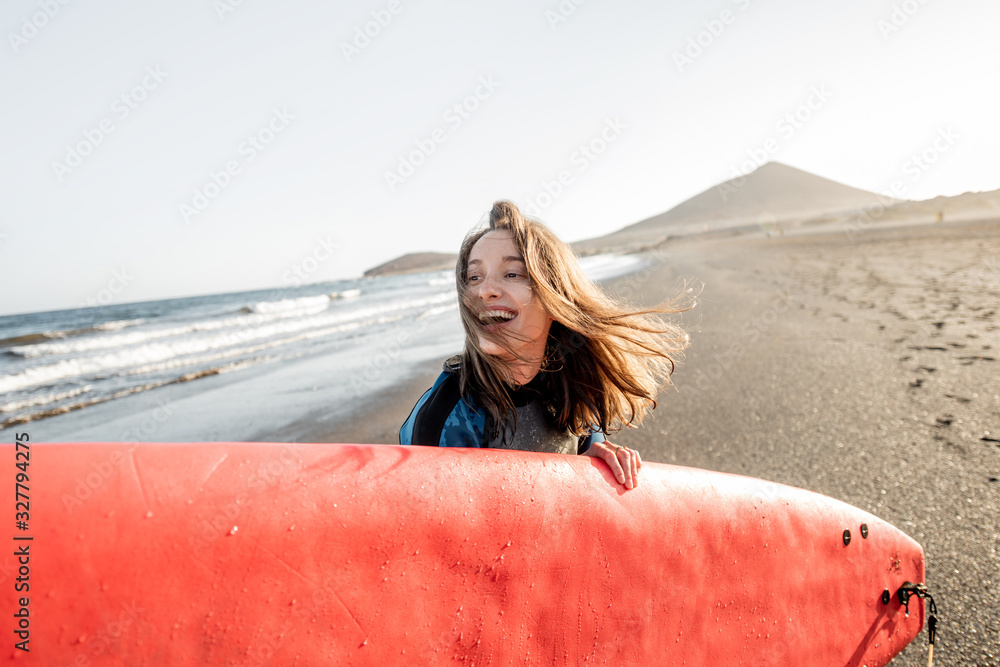 日落时，一位身穿潜水服、拿着冲浪板在海滩上的年轻快乐女性的肖像。W