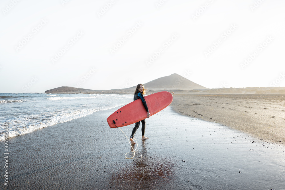 Beautiful sunset view on the ocean beach and surfer walking with red surfboard on a sunset