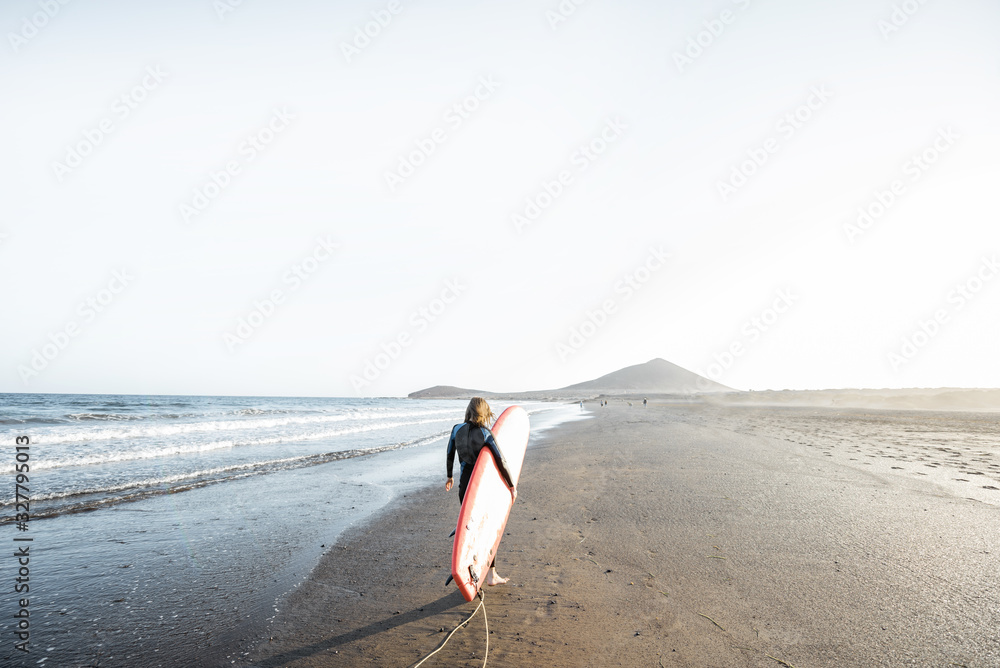 Beautiful sunset view on the ocean beach and surfer walking with red surfboard on a sunset