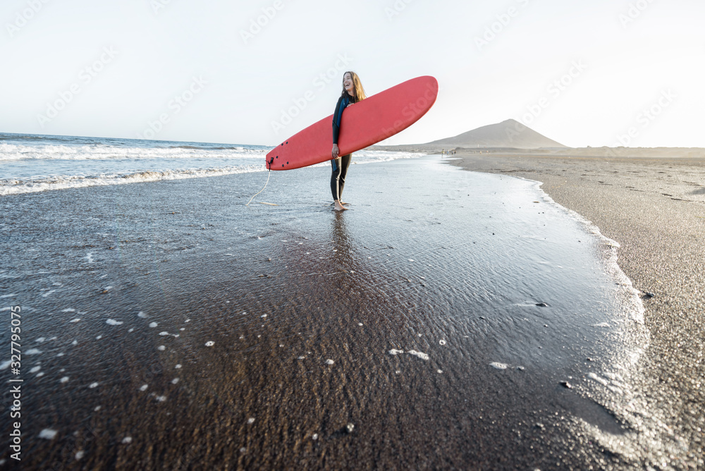 Beautiful sunset view on the ocean beach and surfer walking with red surfboard on a sunset