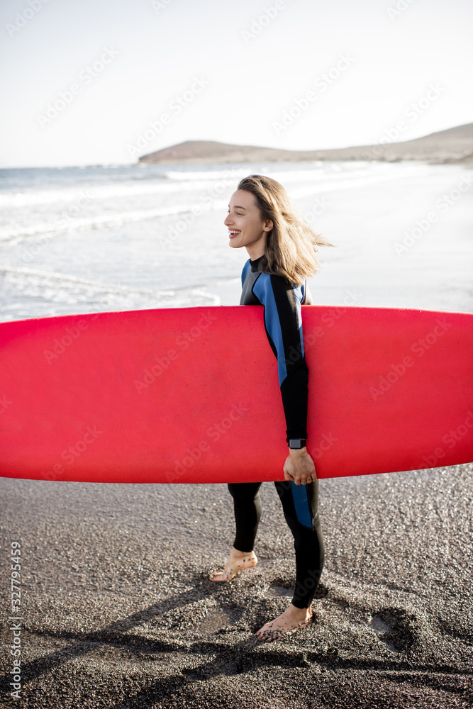 Portrait of a young woman in wetsuit standing with surfboard on the beautiful beach on a sunset. Wat