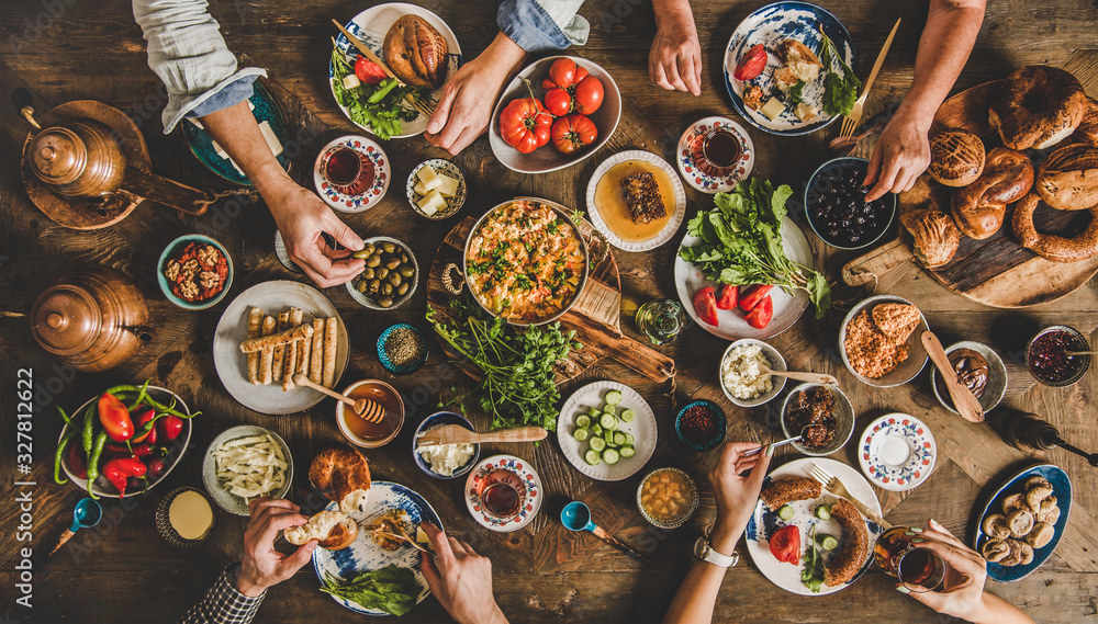 Turkish breakfast. Flat-lay of family eating pastry, vegetables, greens, cheeses, fried eggs, jams f