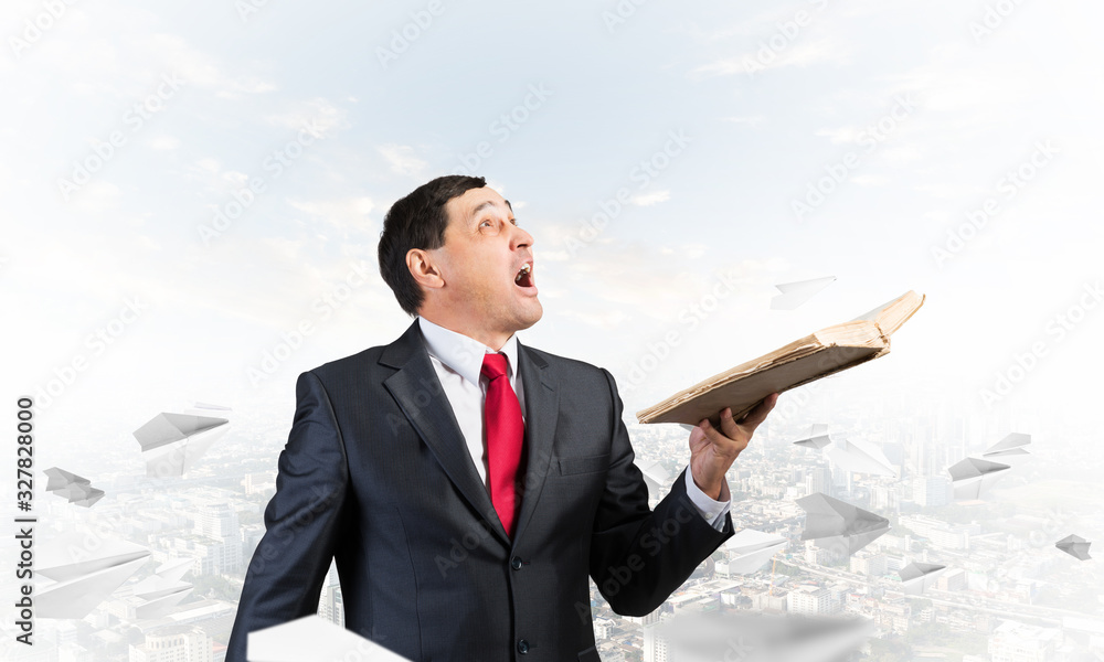 Surprised businessman holding open old book