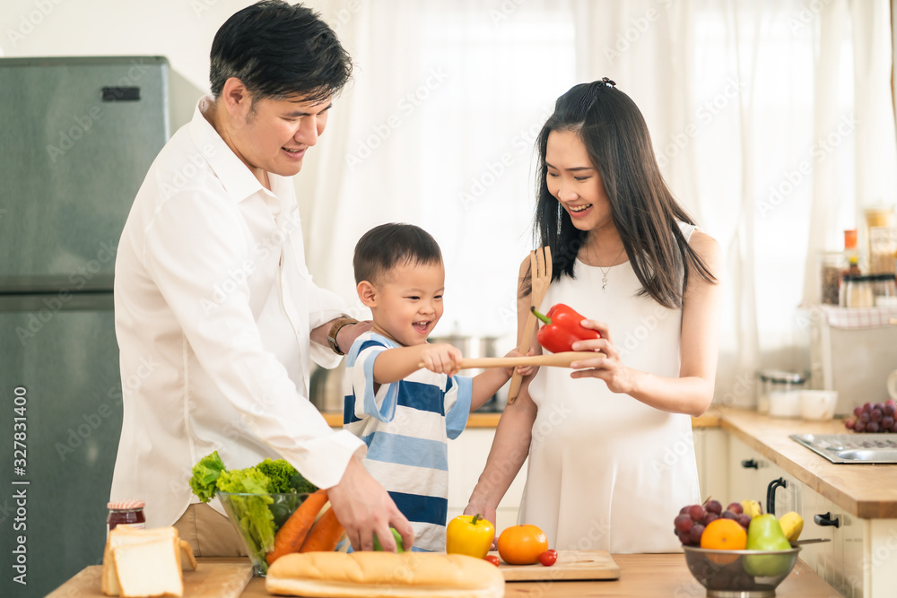 可爱可爱的亚洲家庭在家里的厨房里做食物。微笑的母亲、父亲和孩子的肖像