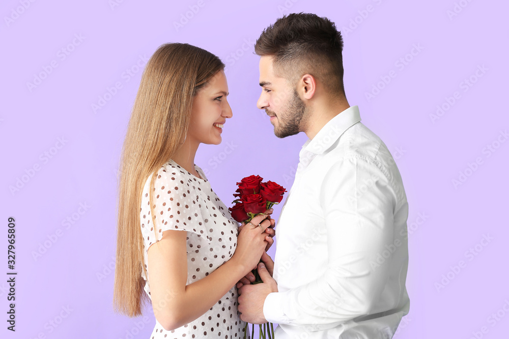 Happy young couple with bouquet of flowers on color background