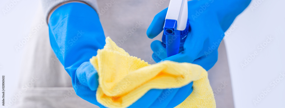 Young woman housekeeper is doing cleaning white table in apron with blue gloves, spray cleaner, wet 