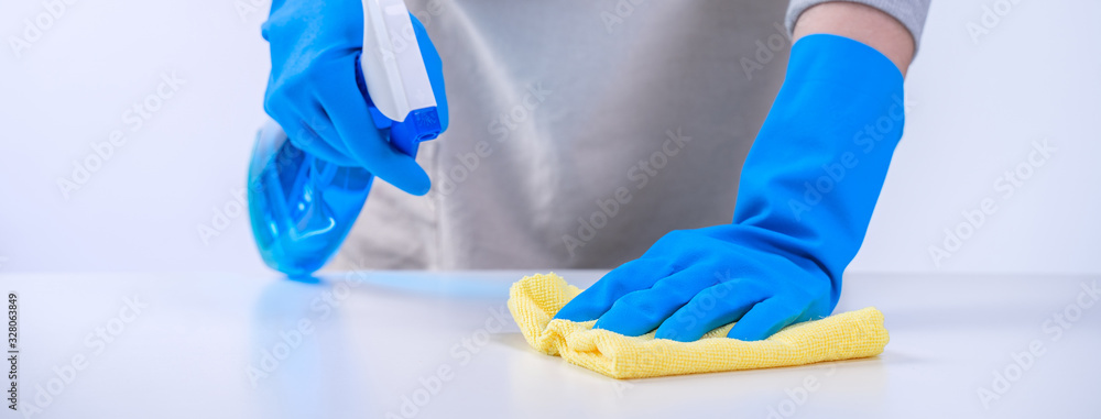 Young woman housekeeper is doing cleaning white table in apron with blue gloves, spray cleaner, wet 