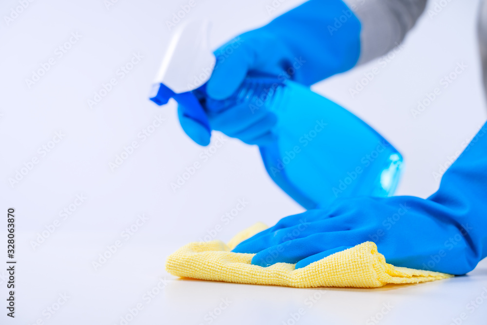 Young woman housekeeper is doing cleaning white table in apron with blue gloves, spray cleaner, wet 