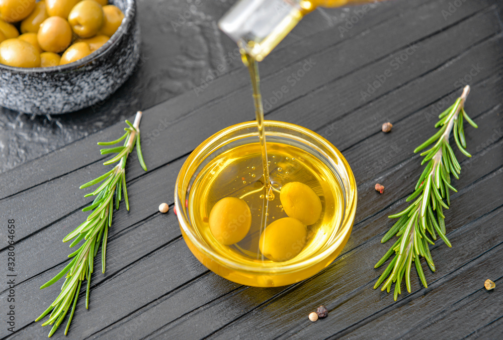 Pouring of tasty olive oil from bottle into bowl on table