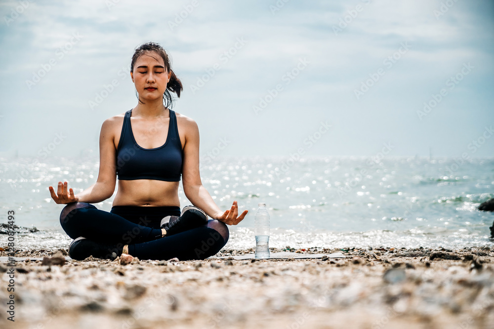 Young Asian woman practicing yoga exercise at quiet rock pier with sea background. Sport and recreat