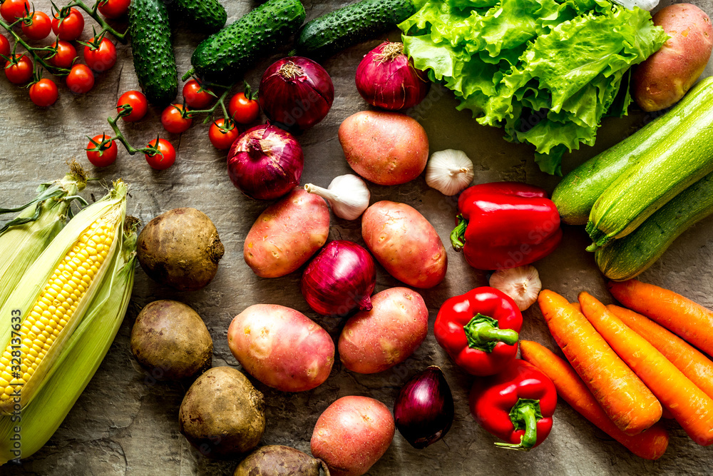 Fresh vegetables still life. Potato, cucumber, beet carrot, greenery on stone background top-down