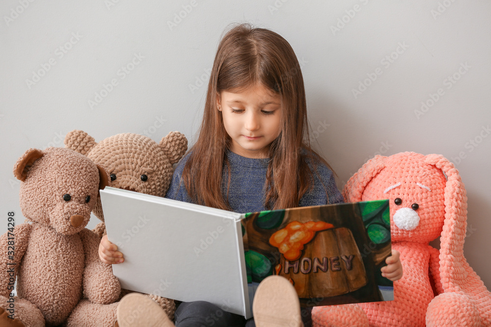 Cute little girl with toys reading book at home