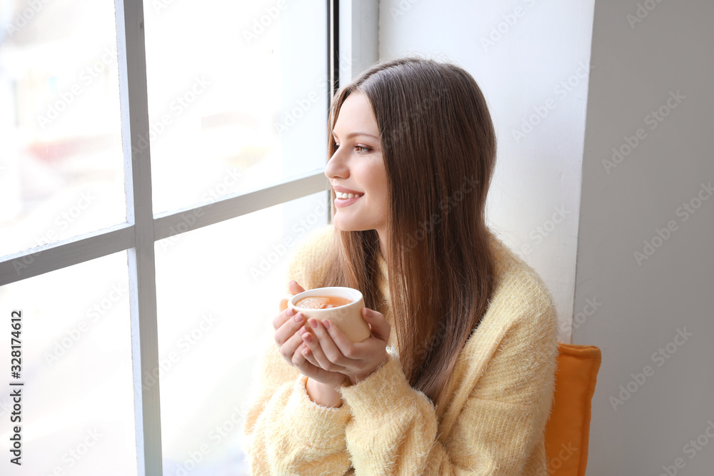 家里窗台上坐着一杯茶的漂亮年轻女人