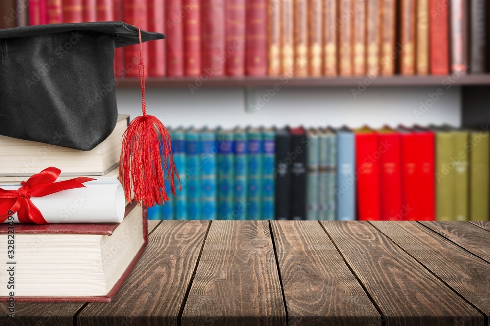 Graduation cap with stack books on wooden desk