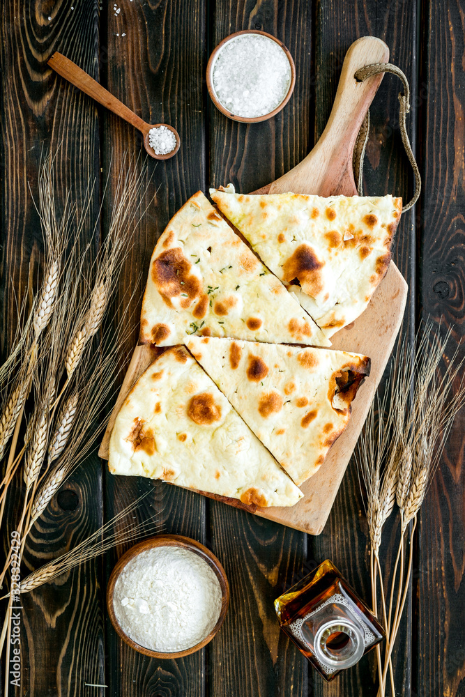 Focaccia ingredients. Wheat ears, flour, oil near bread on dark wooden background top-down