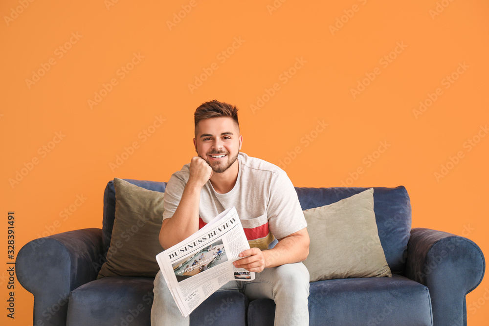 Young man reading newspaper while sitting on sofa at home