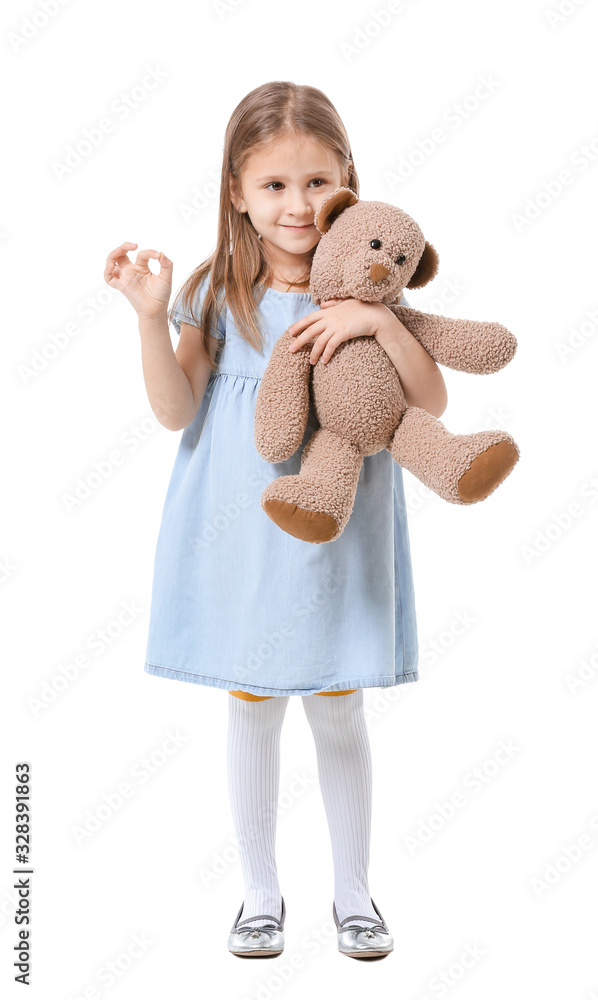 Cute little girl with teddy bear showing OK gesture on white background