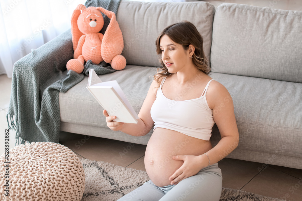 Beautiful pregnant woman reading book at home