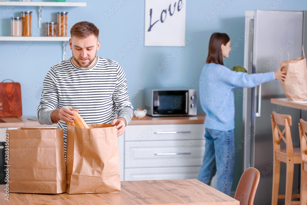 Young couple unpacking fresh products from market in kitchen