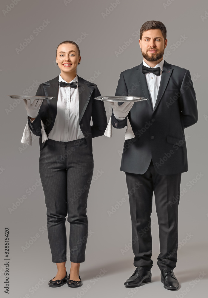 Male and female waiters on grey background